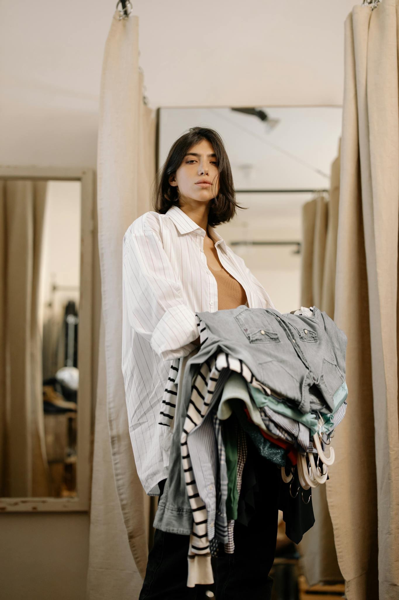Woman stands in fitting room holding clothes and looking confident in a clothing store.